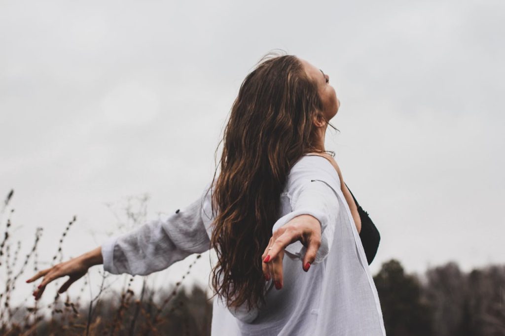 A woman with long hair joyfully embracing nature in an open field.